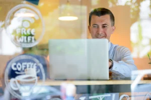 A businessman working on a laptop in a café environment using guest Wi-Fi for remote work.