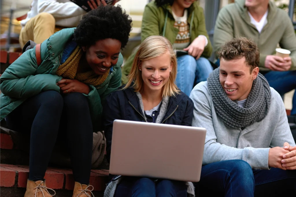 University students working together on a laptop outdoors using university guest WiFi for group study and online learning on campus