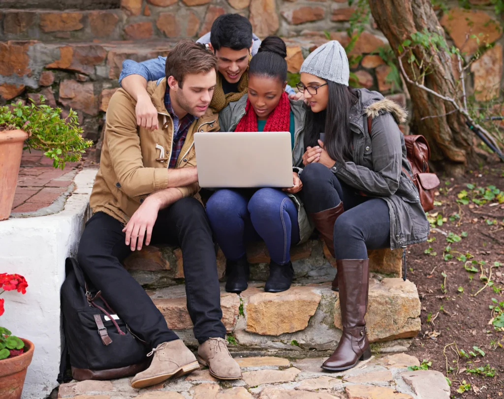 University students working together on a laptop outdoors using university guest WiFi for group study and online learning on campus